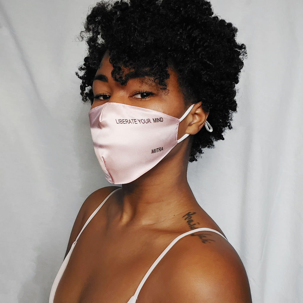 Woman wearing a pink silk face mask that says liberate your mind on it