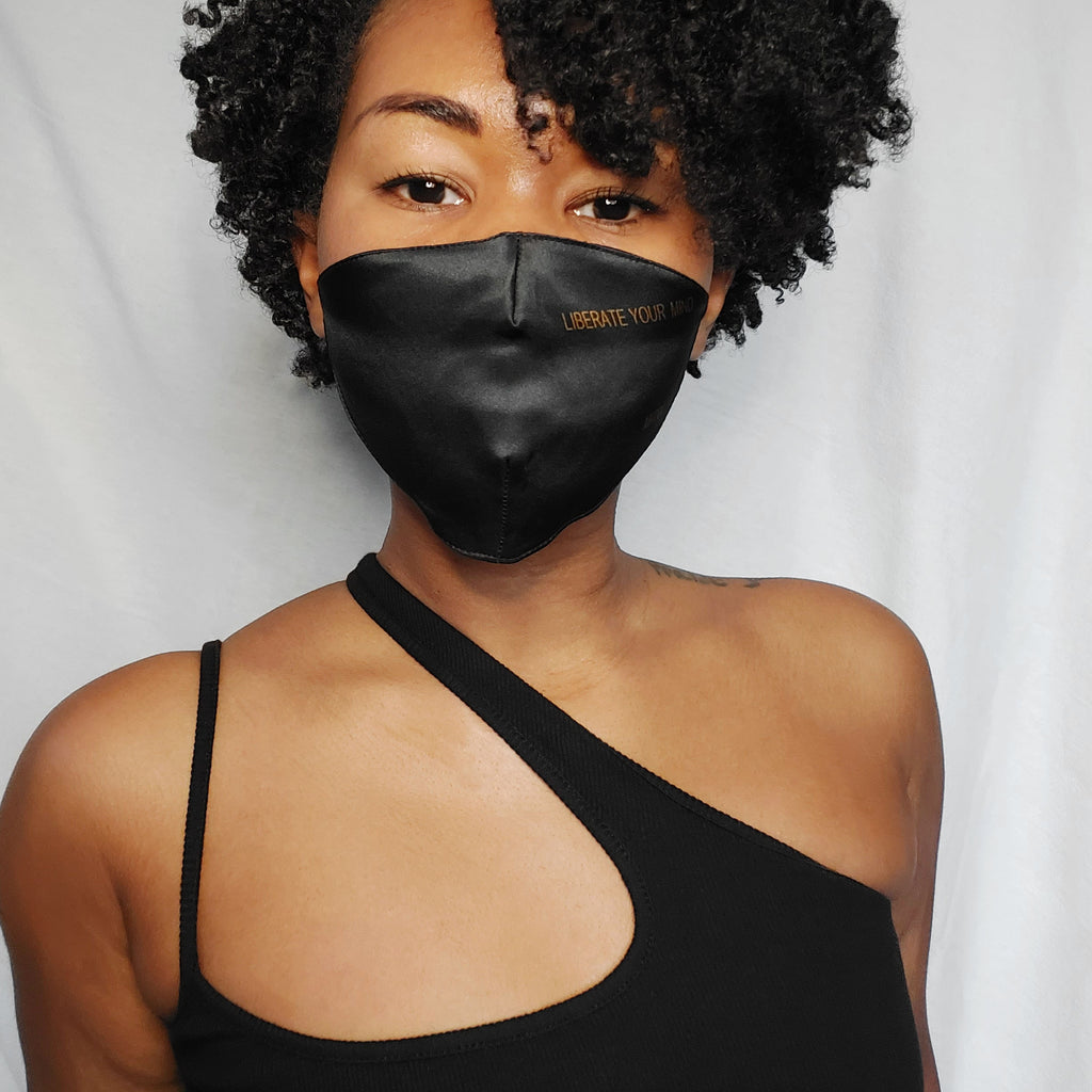 Woman wearing a black silk face mask that says liberate your mind on it