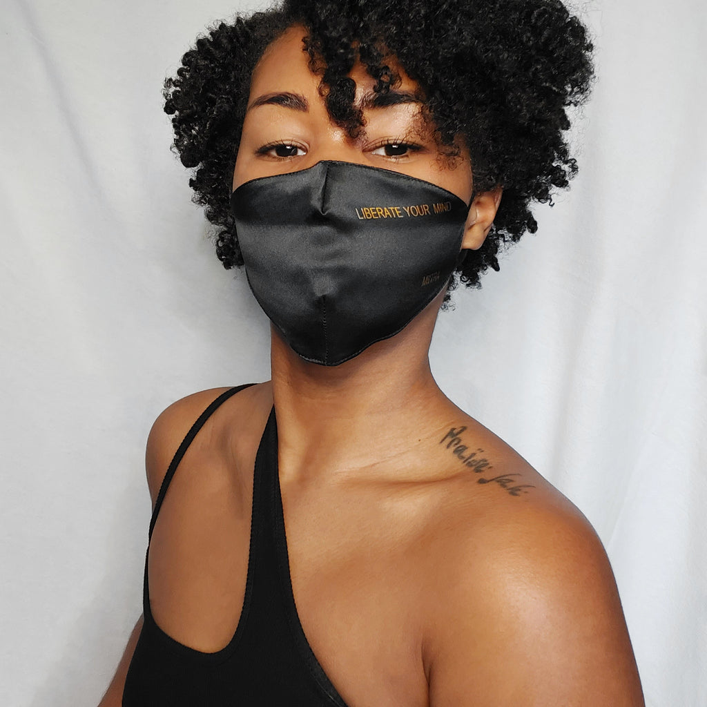 Woman wearing a black silk face mask that says liberate your mind on it