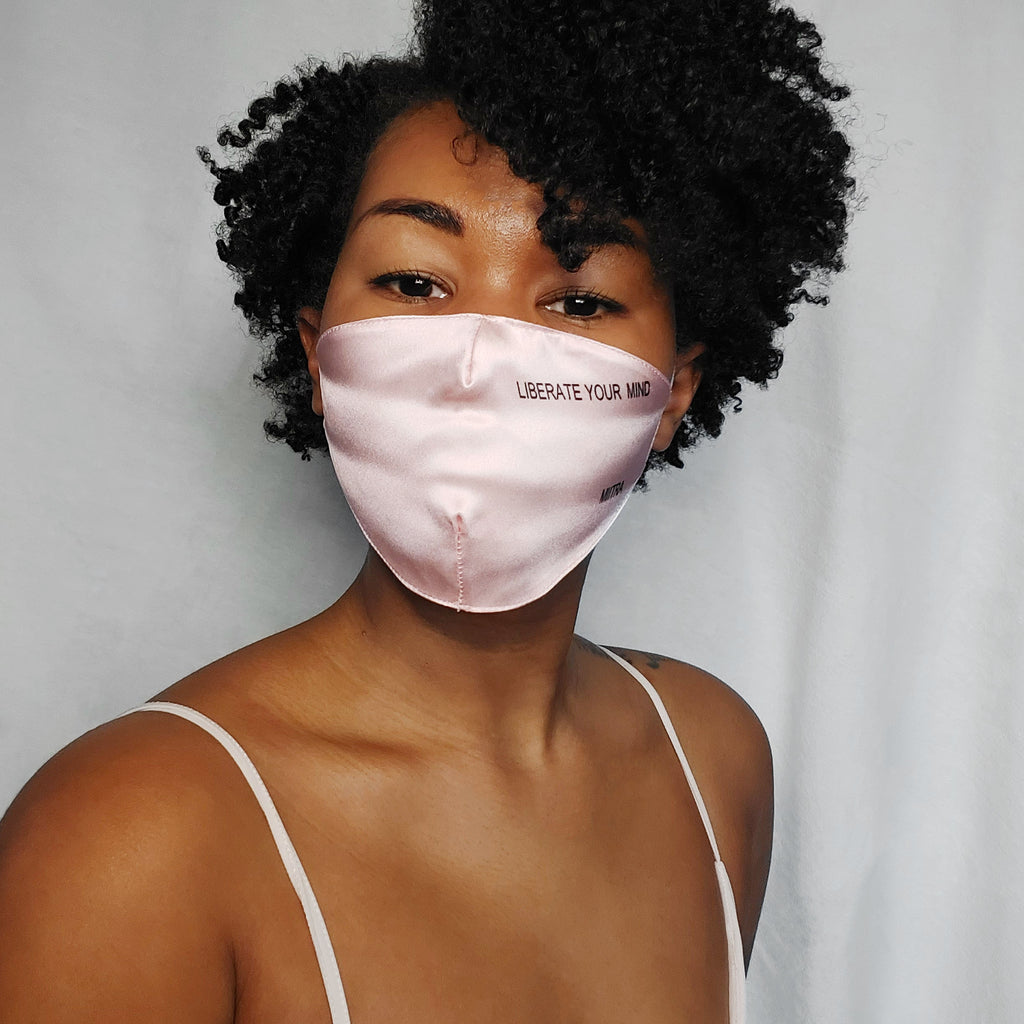 Woman wearing a pink silk face mask that says liberate your mind on it